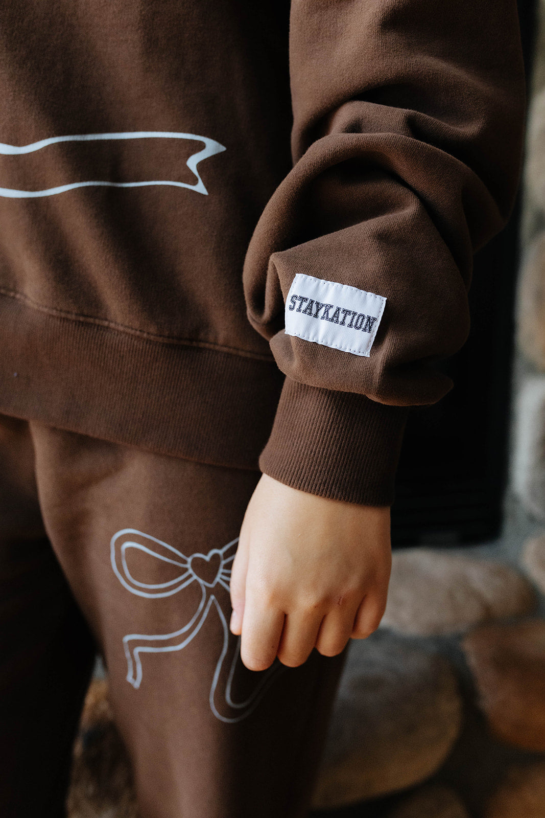 Close view of the brown bow sweatshirt cuff and bow graphic on the sweatpants.