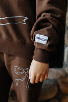 Close view of the brown bow sweatshirt cuff and bow graphic on the sweatpants.