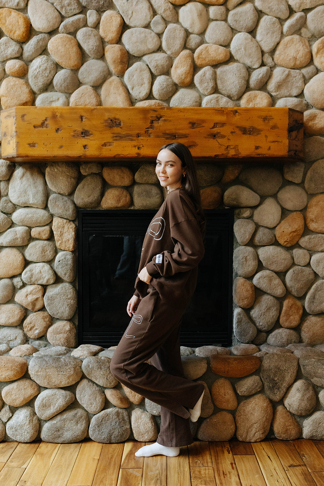Side and back view of the brown bow sweatshirt and sweatpants by a fireplace.