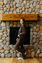Side and back view of the brown bow sweatshirt and sweatpants by a fireplace.