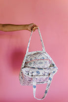 Person holding a patterned bag against a pink background
