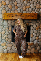 Full length front view of the adult brown bow print short sleeve pajama set by a fireplace.