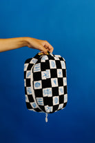 Black and white checkered bag with blue patterns held by a hand against a blue background