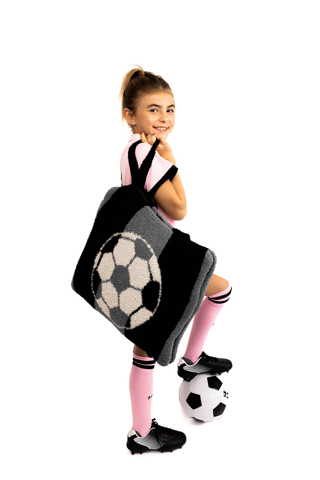 Child holding a soccer-themed quillow with a soccer ball design on a white background