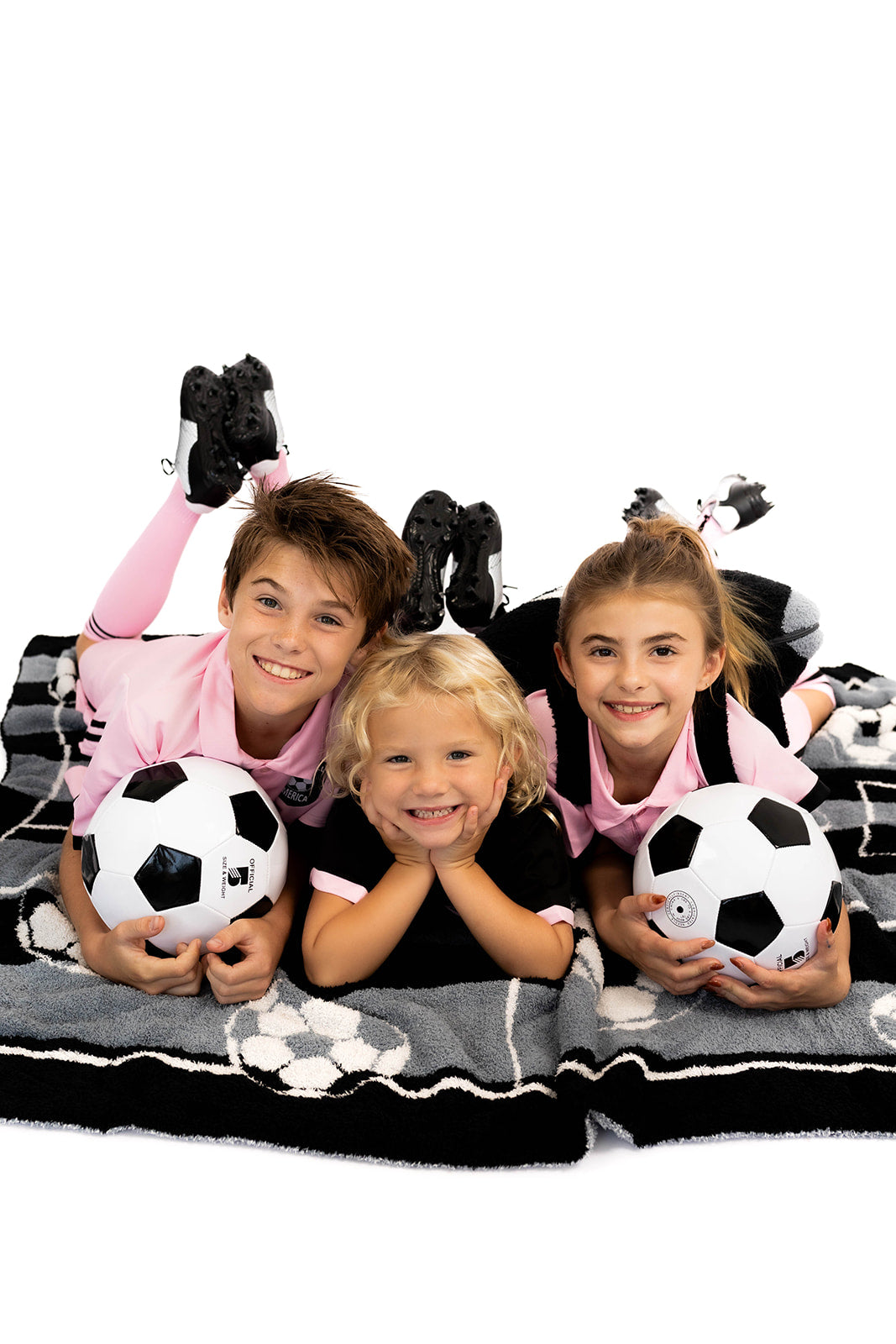 Three children with soccer balls on a white background laying on soccer blanket