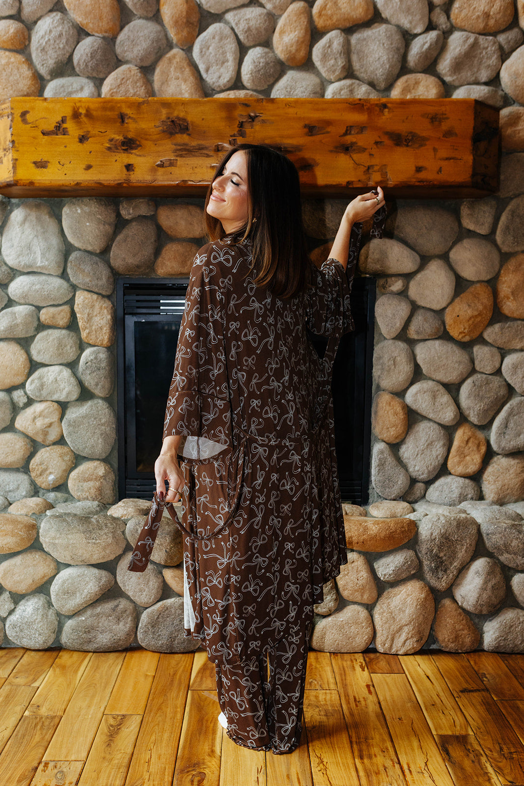 Back view of the brown bow print robe by a stone fireplace.