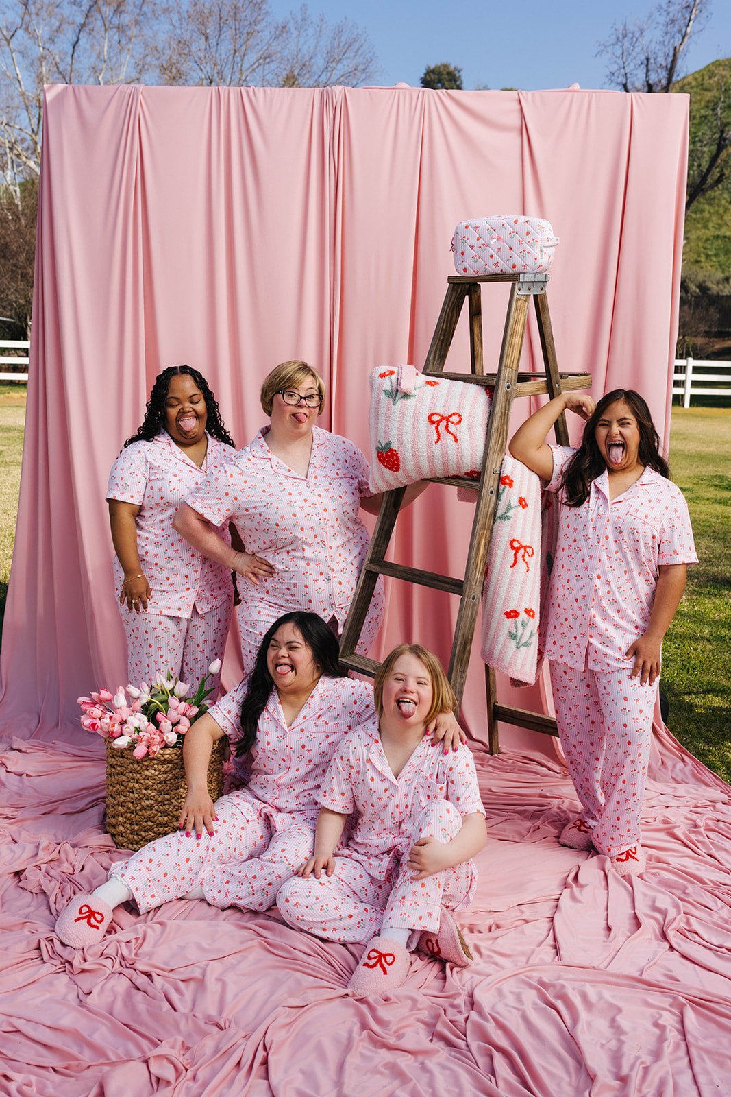 Group of people in matching pajamas posing in front of a pink backdrop with a ladder and decorative items.
