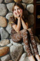 Child wearing the brown bow print pajama set by a stone fireplace.
