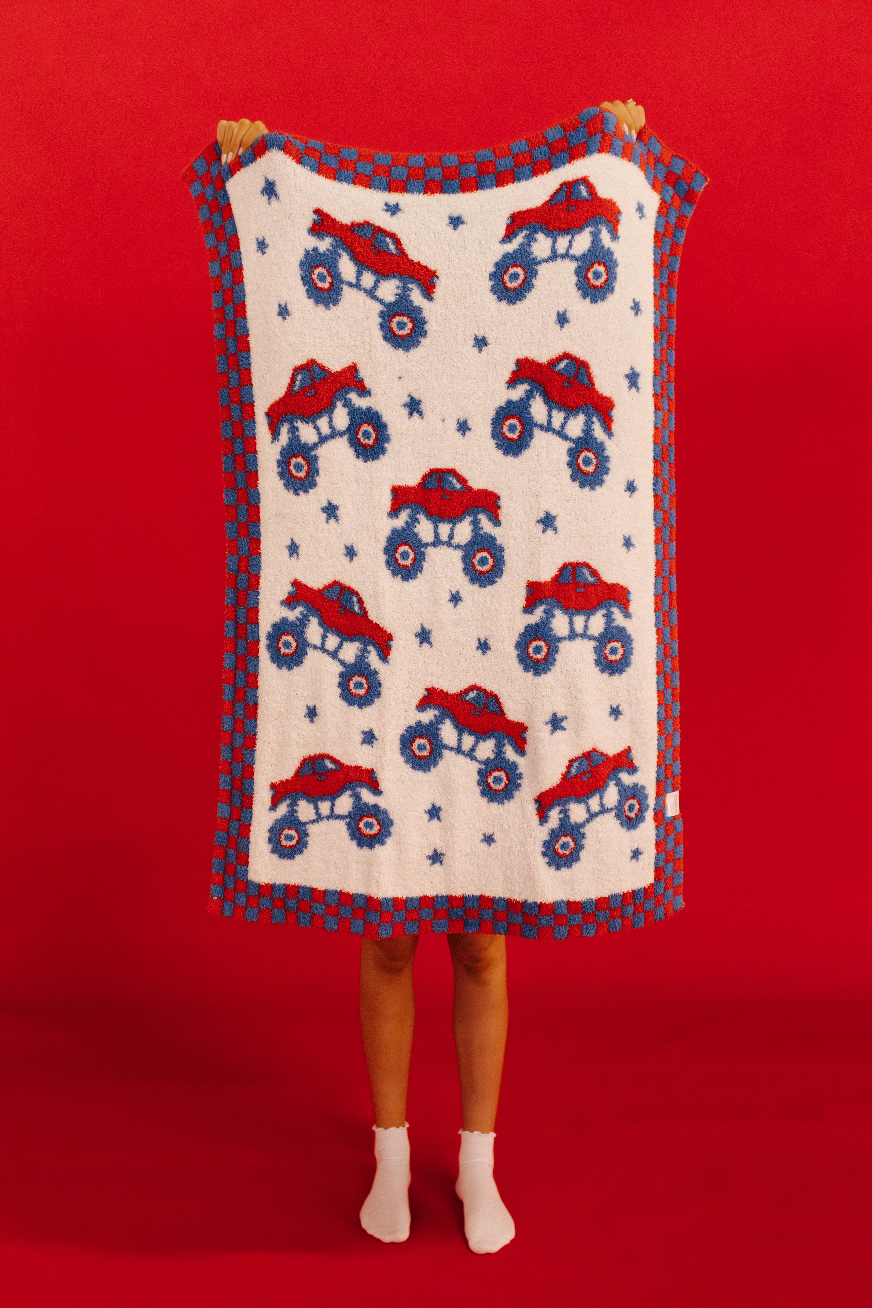 Person holding a blanket with monster truck pattern against a red background
