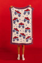 Person holding a blanket with monster truck pattern against a red background
