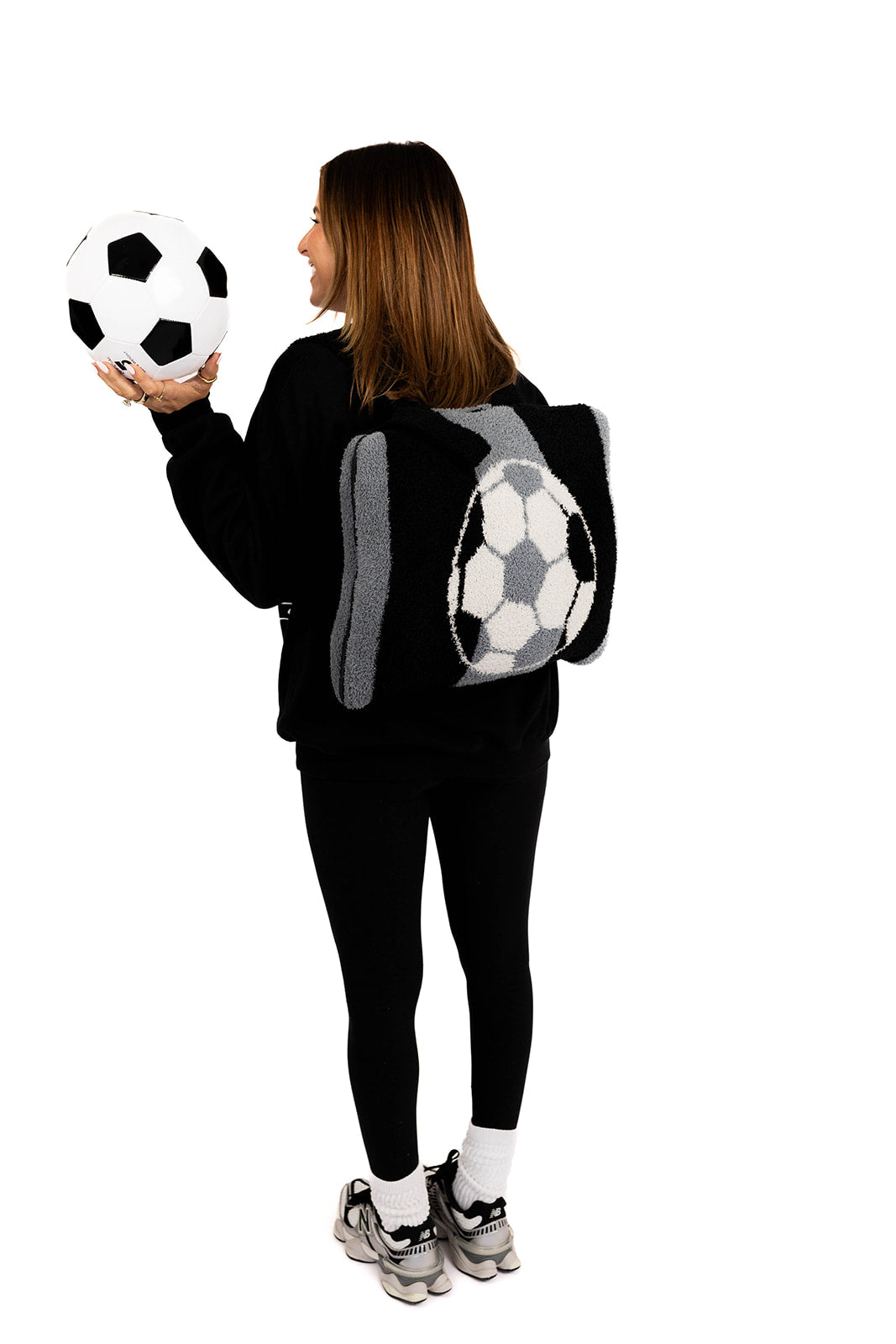 Person wearing a black outfit with a soccer ball quillow on their back against a white background