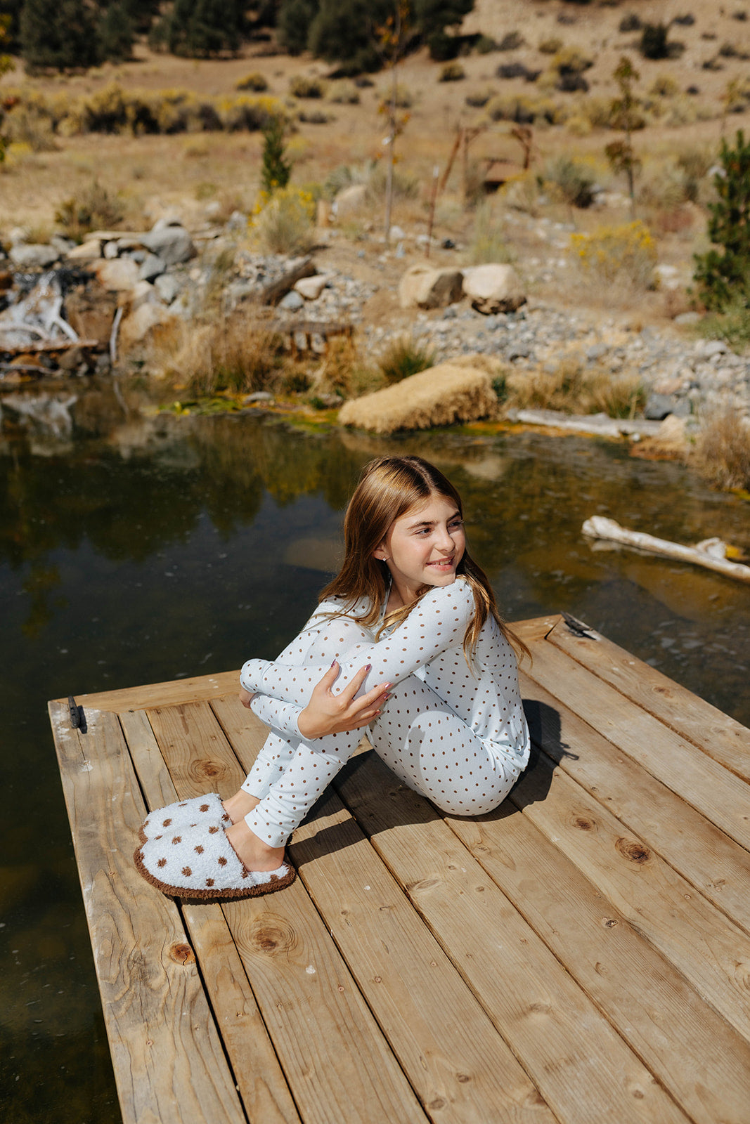 Child wearing the light blue pajamas with small brown polka dots while seated on a dock.