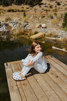 Child wearing the light blue pajamas with small brown polka dots while seated on a dock.
