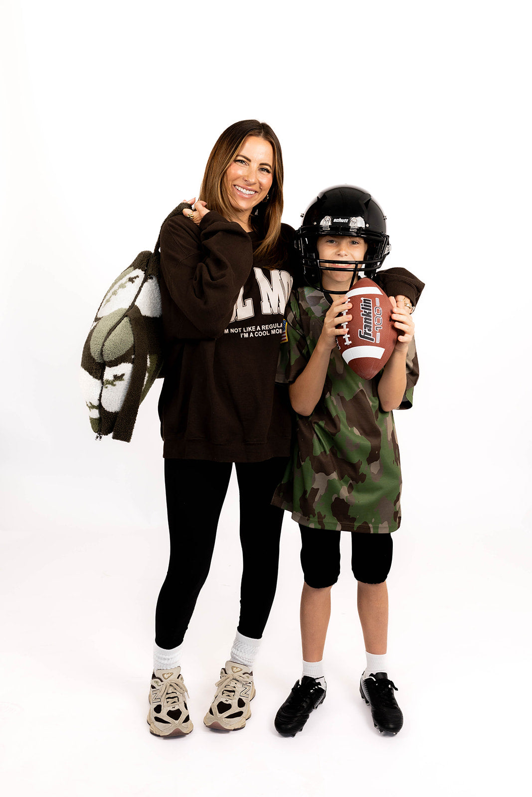 Woman and child in football outfit holding football and football quillow standing together on a white background