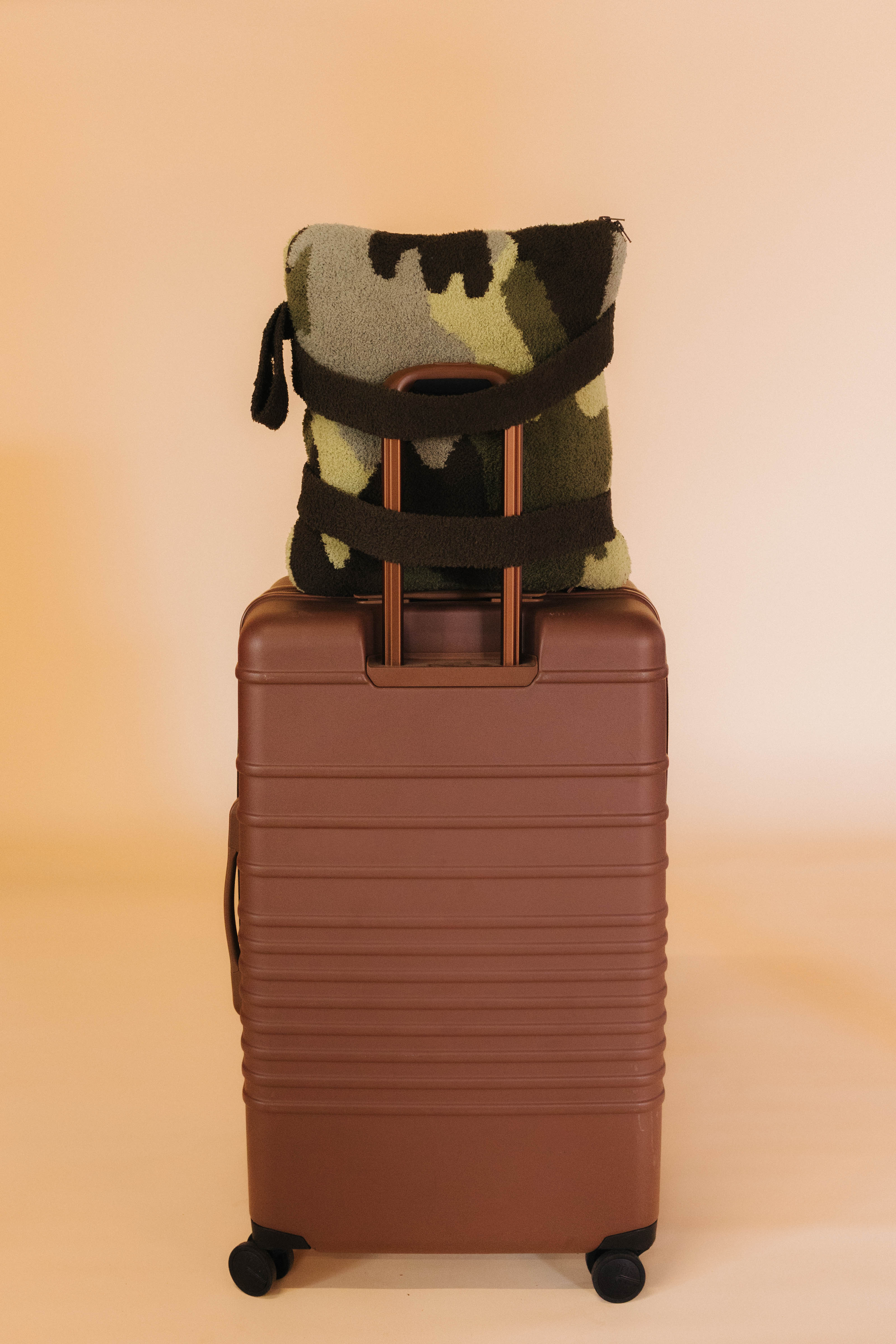 Camouflage-patterned quillow on top of a brown suitcase against a beige background
