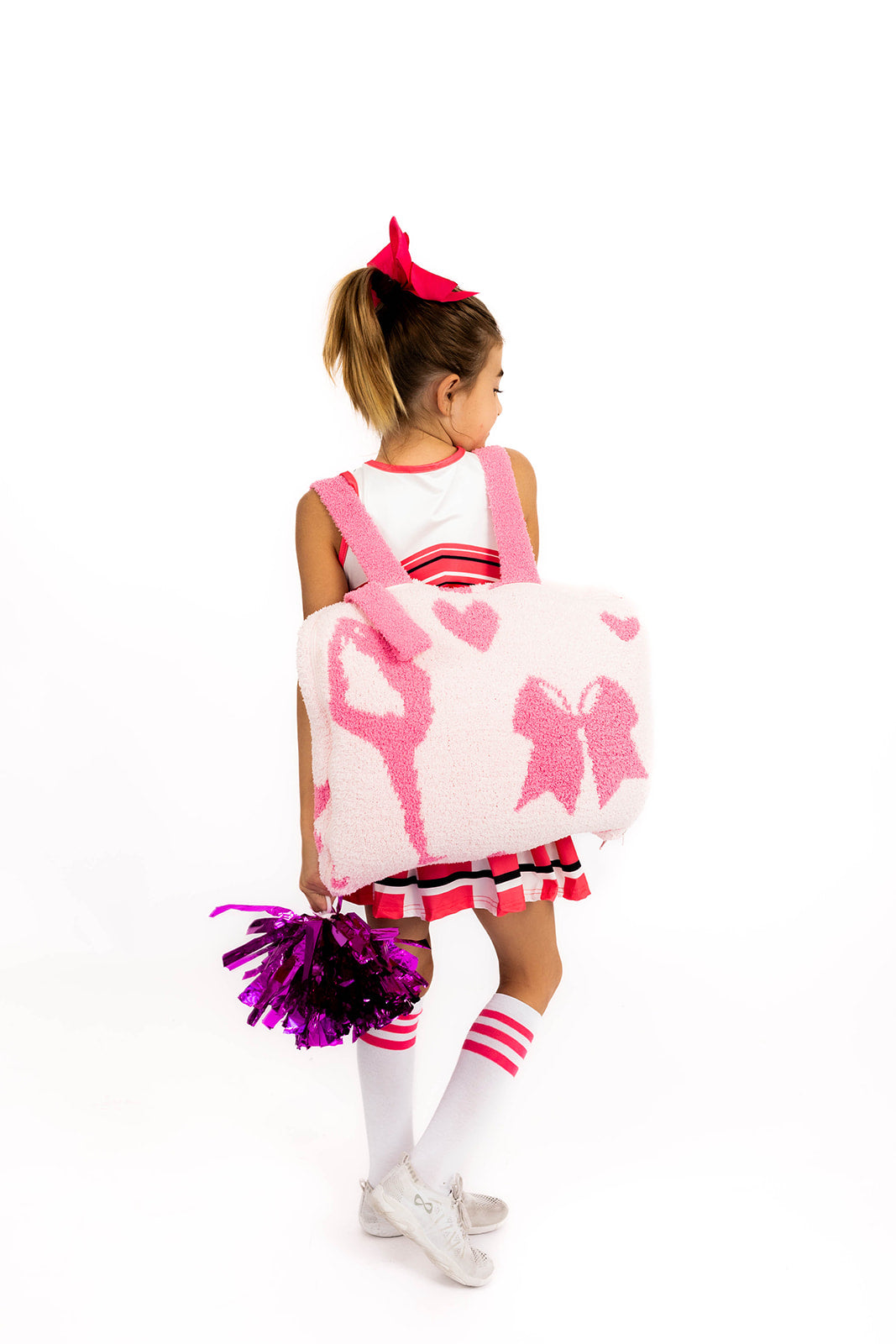 Child in a cheerleading outfit holding a pink and white quillow with cheerleading graphics on a white background