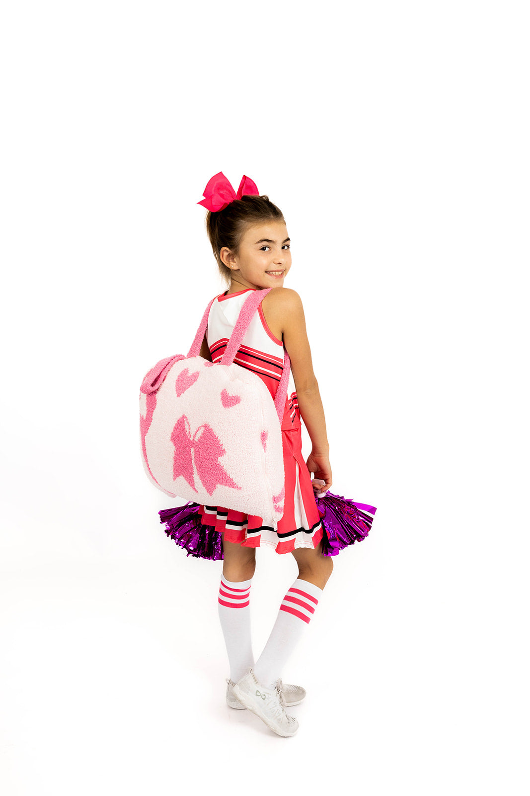 Child wearing a pink and white cheerleading outfit with a backpack cheer quillow on a white background
