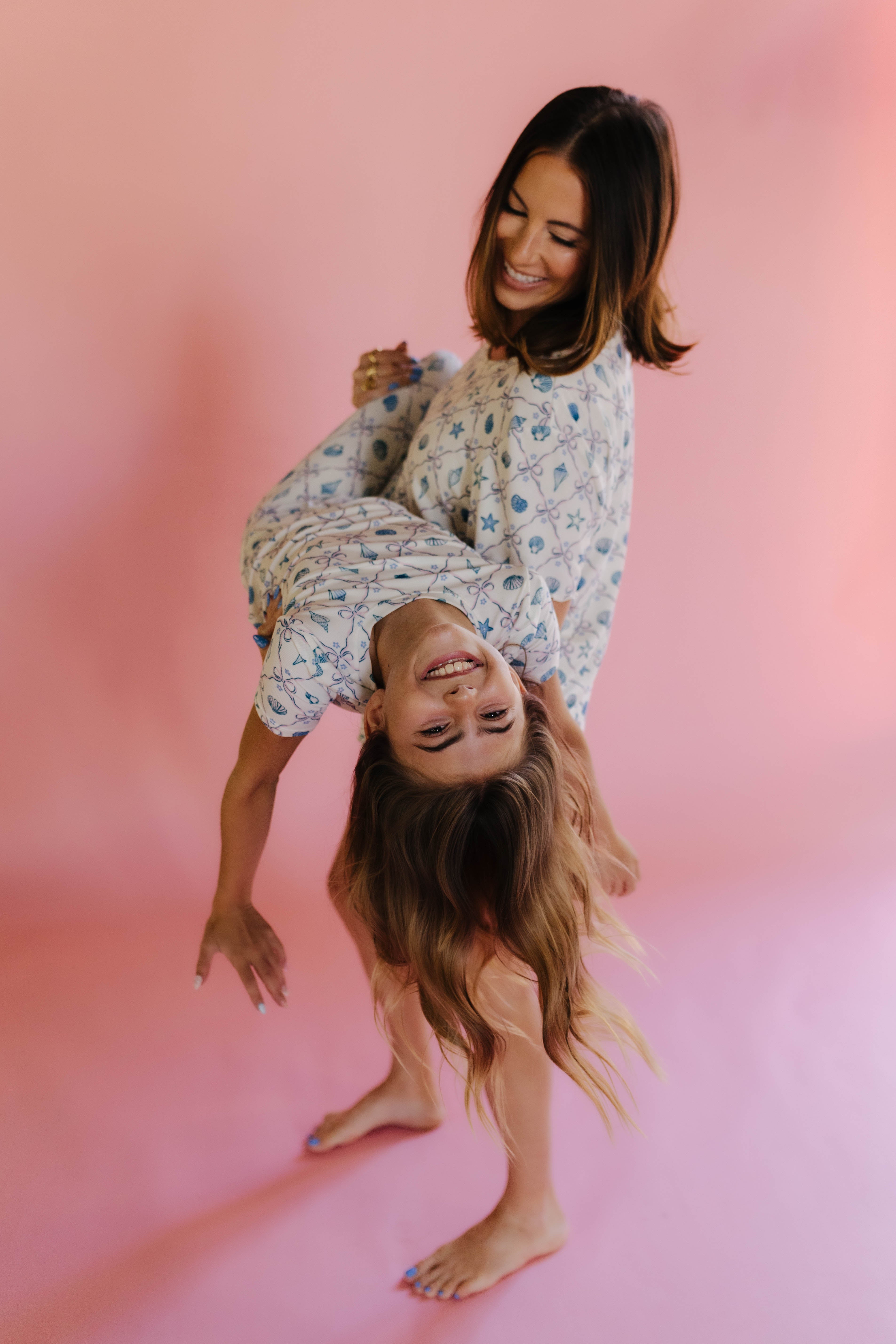 Two women in matching shell outfits standing on a pink background