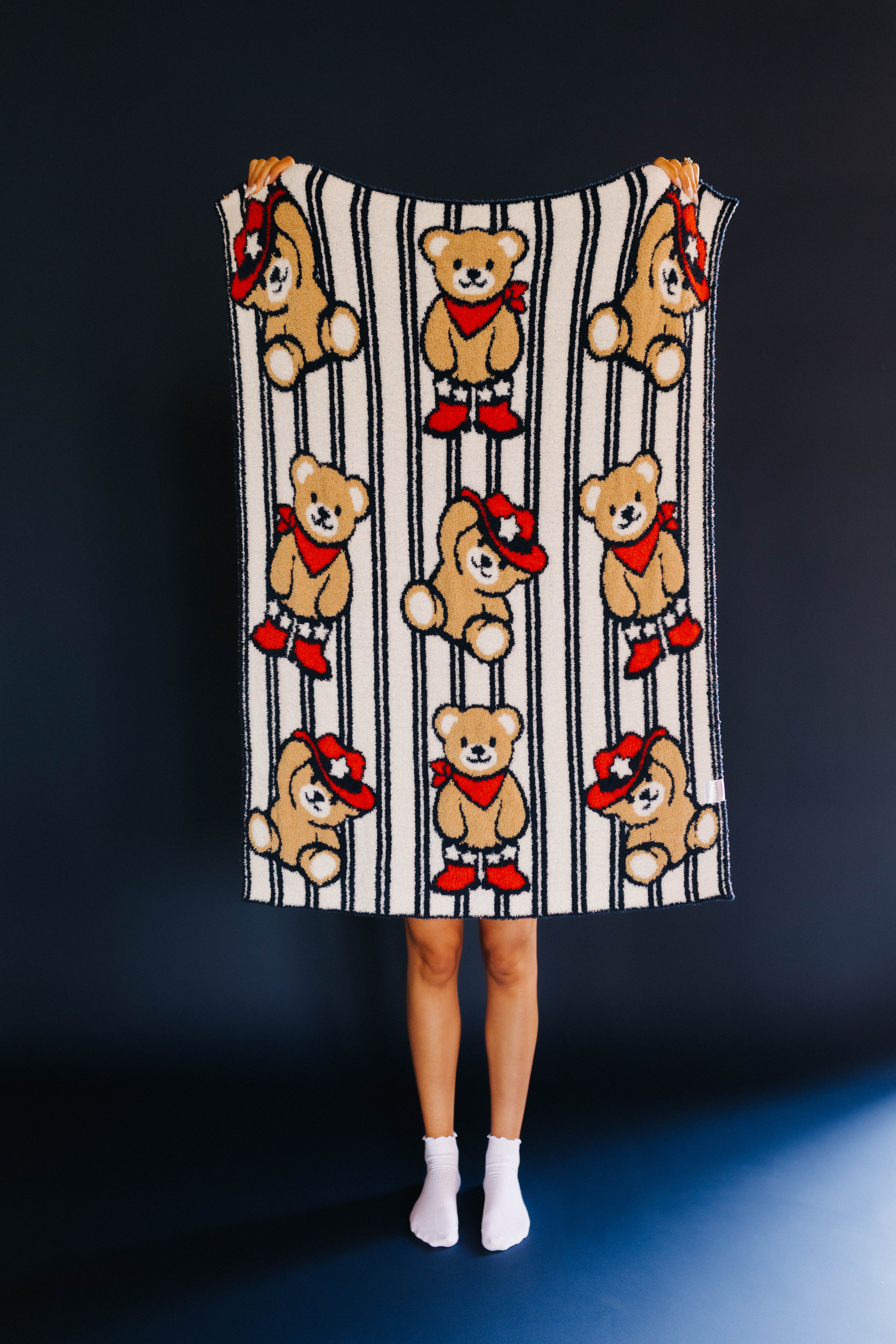 person holding up kid blanket with stripes and teddy bears on it