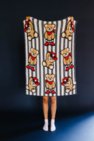 person holding up kid blanket with stripes and teddy bears on it
