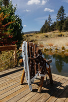 Brown fluffy polka dot robe draped over a wooden chair beside a pond.