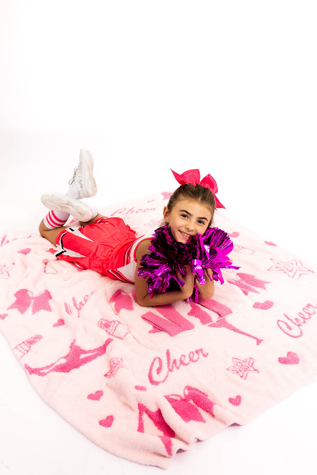 Child in cheerleading outfit with pom-poms on a pink 'Cheer' blanket