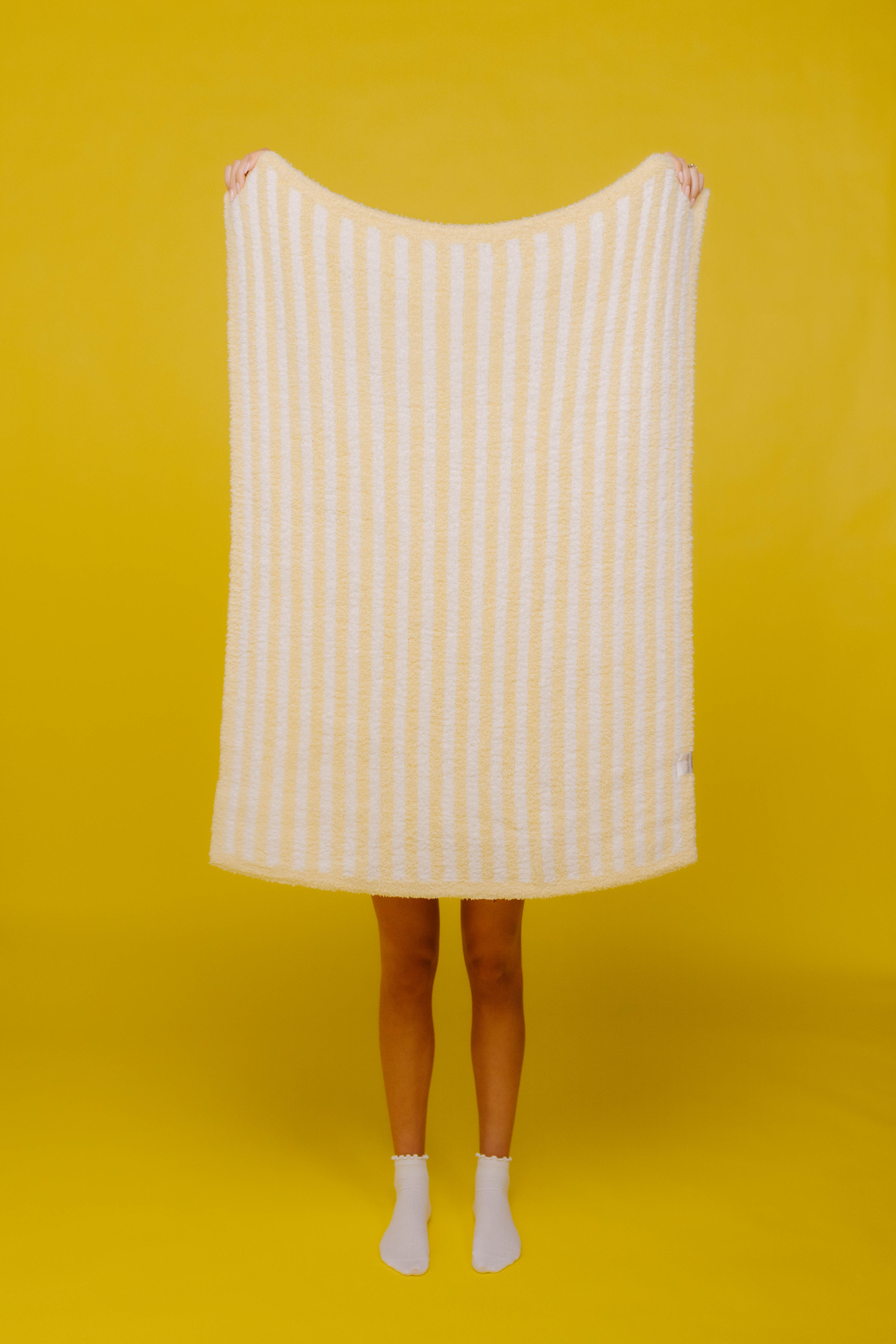 holding up butter yellow stripes baby blanket on yellow background