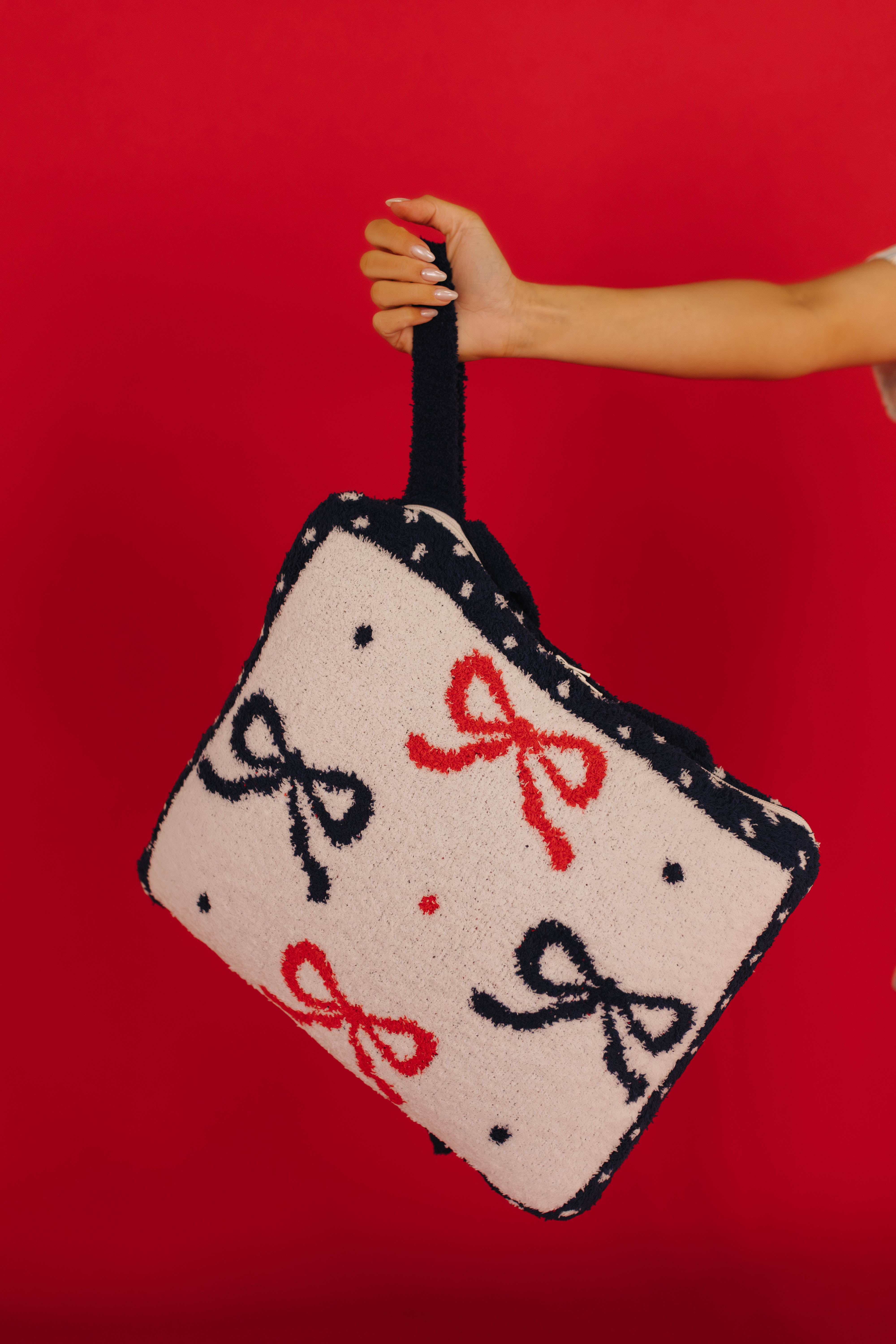 Hand holding a quillow with bow patterns against a red background