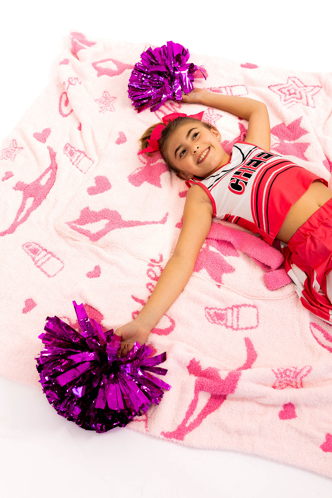 Girl in a cheerleading outfit with pom-poms on a pink cheerleading blanket