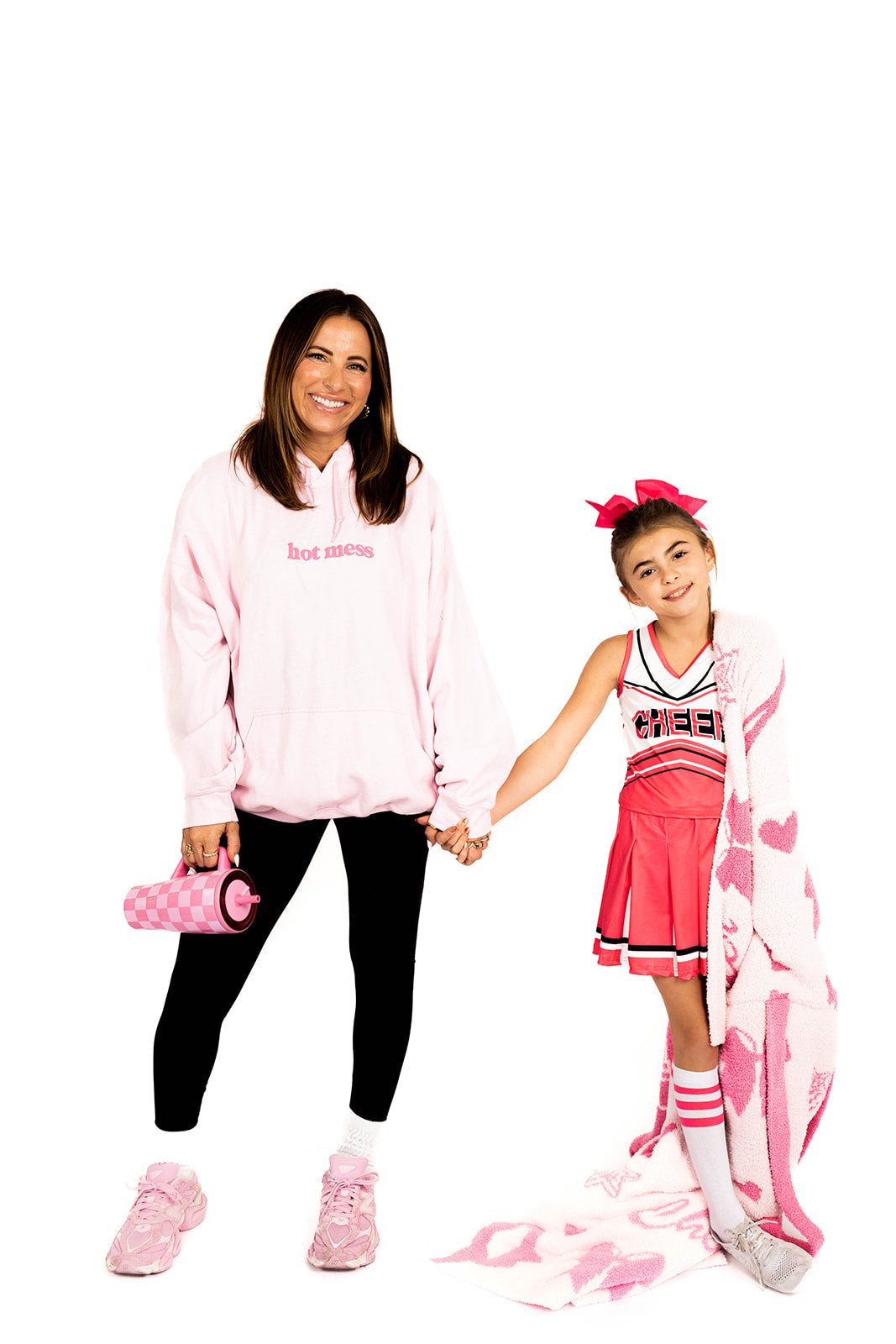 Woman and young girl in pink and black outfits on a white background with cheerleading blanket 