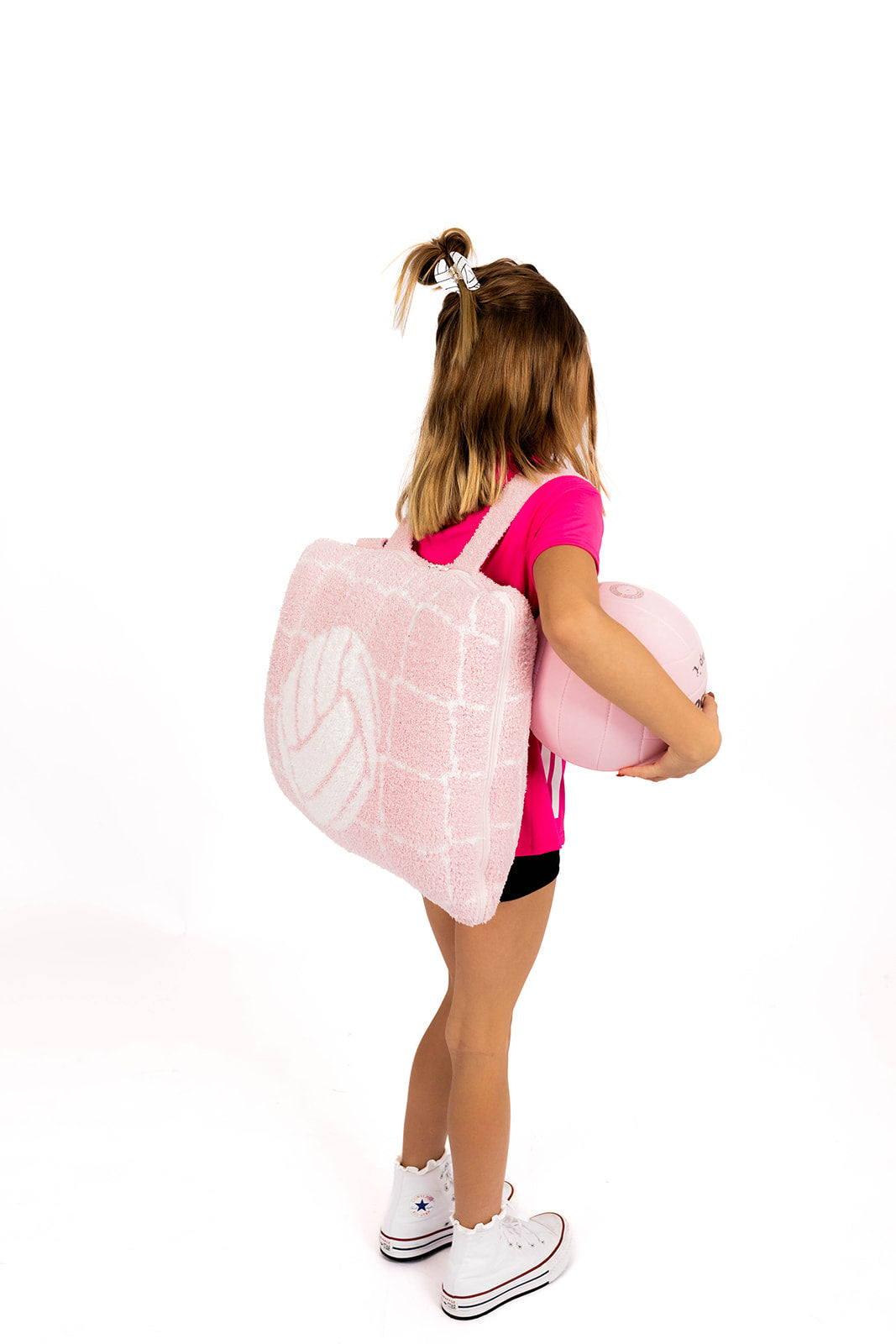Person wearing a pink backpack quillow with white volleyball design on a white background