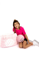 Person holding a pink volleyball and posing with a pink quillow with white volleyball design on a white background