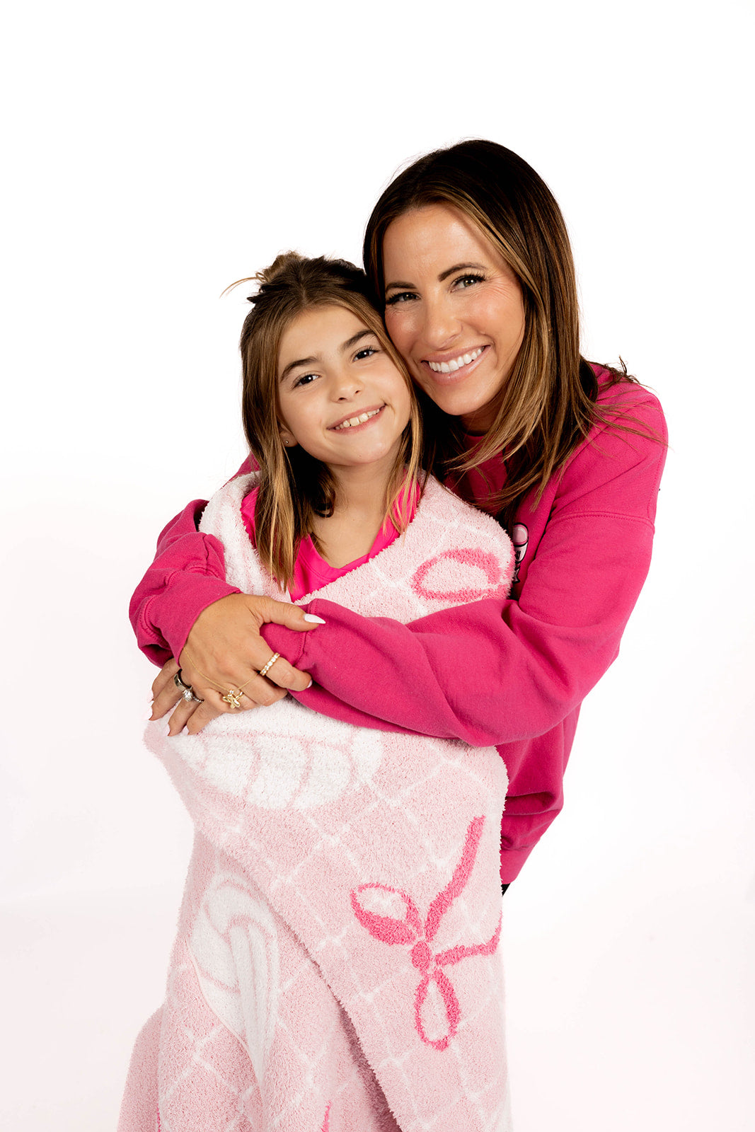 Woman and child wrapped in a pink blanket with volleyball and bow designs on a white background
