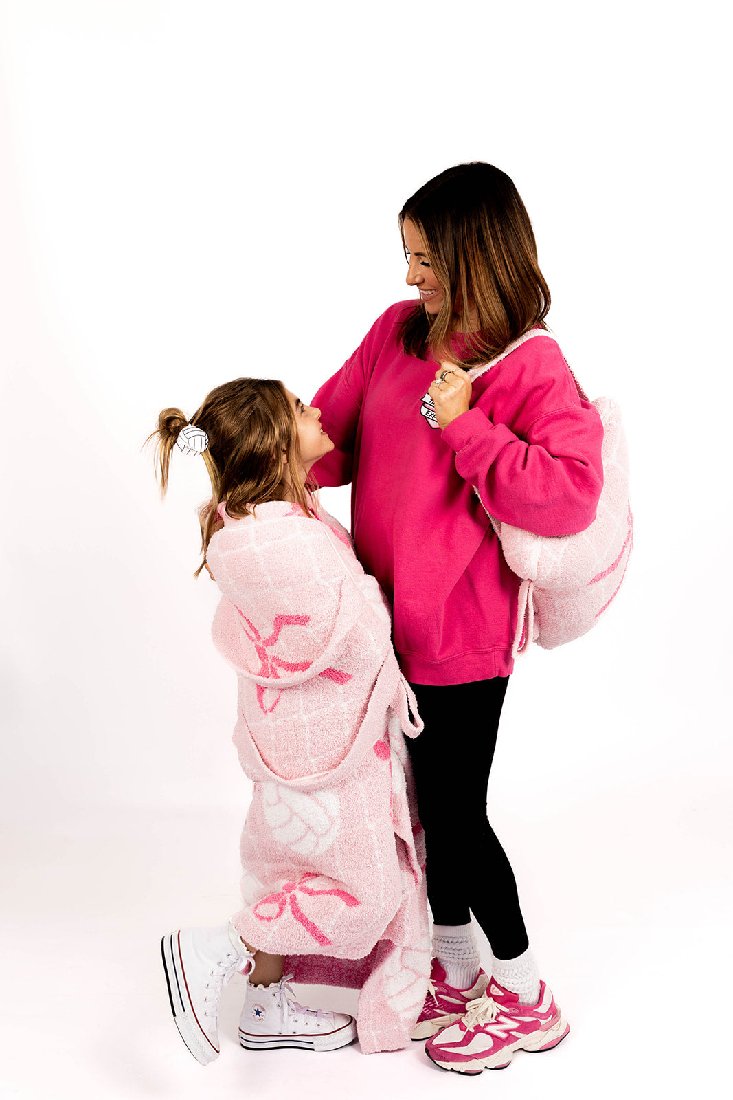 Woman and child holding pink volleyball quillow and wearing volleyball blanket on a white background 