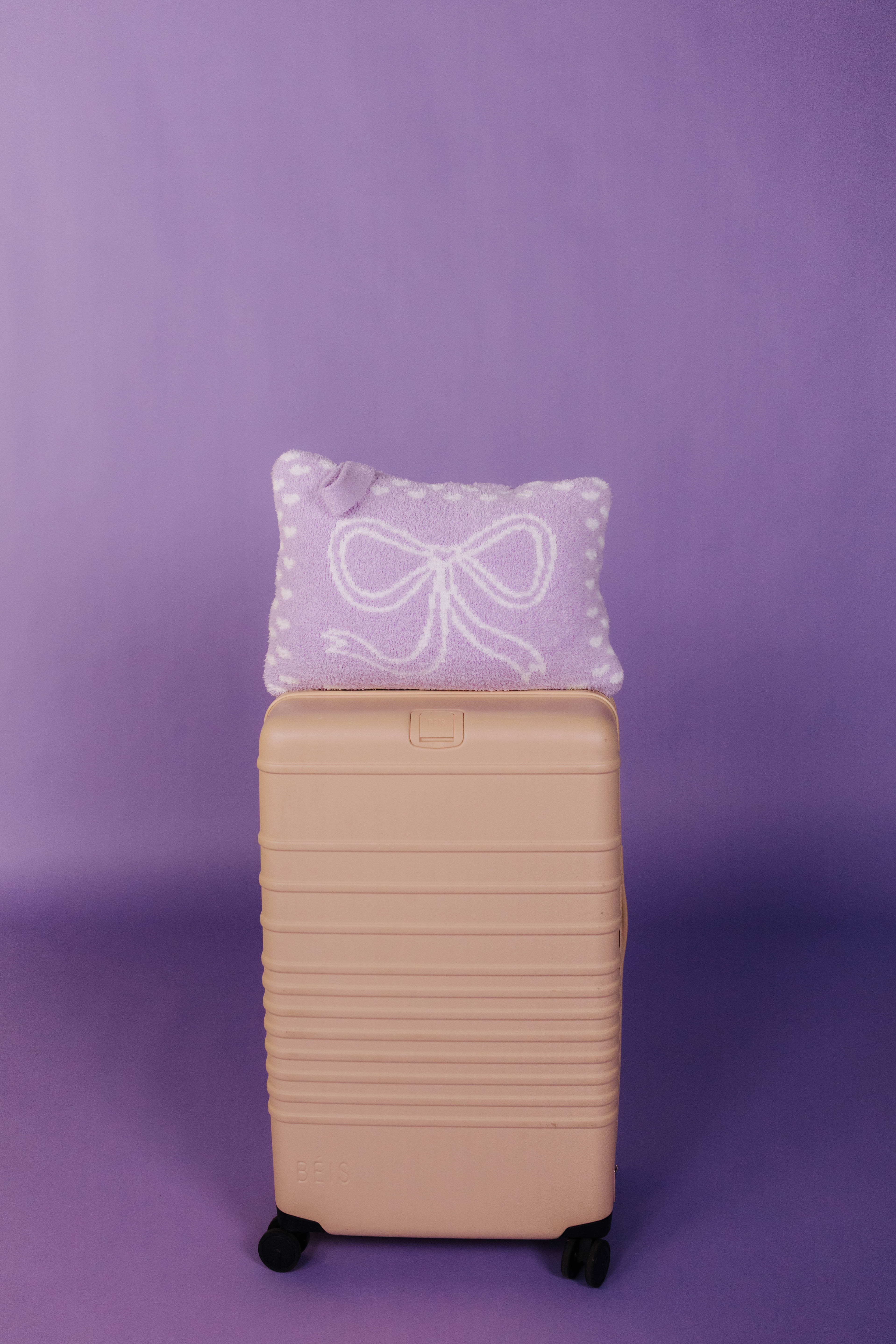 Beige suitcase with a purple quillow featuring a white bow on a purple background