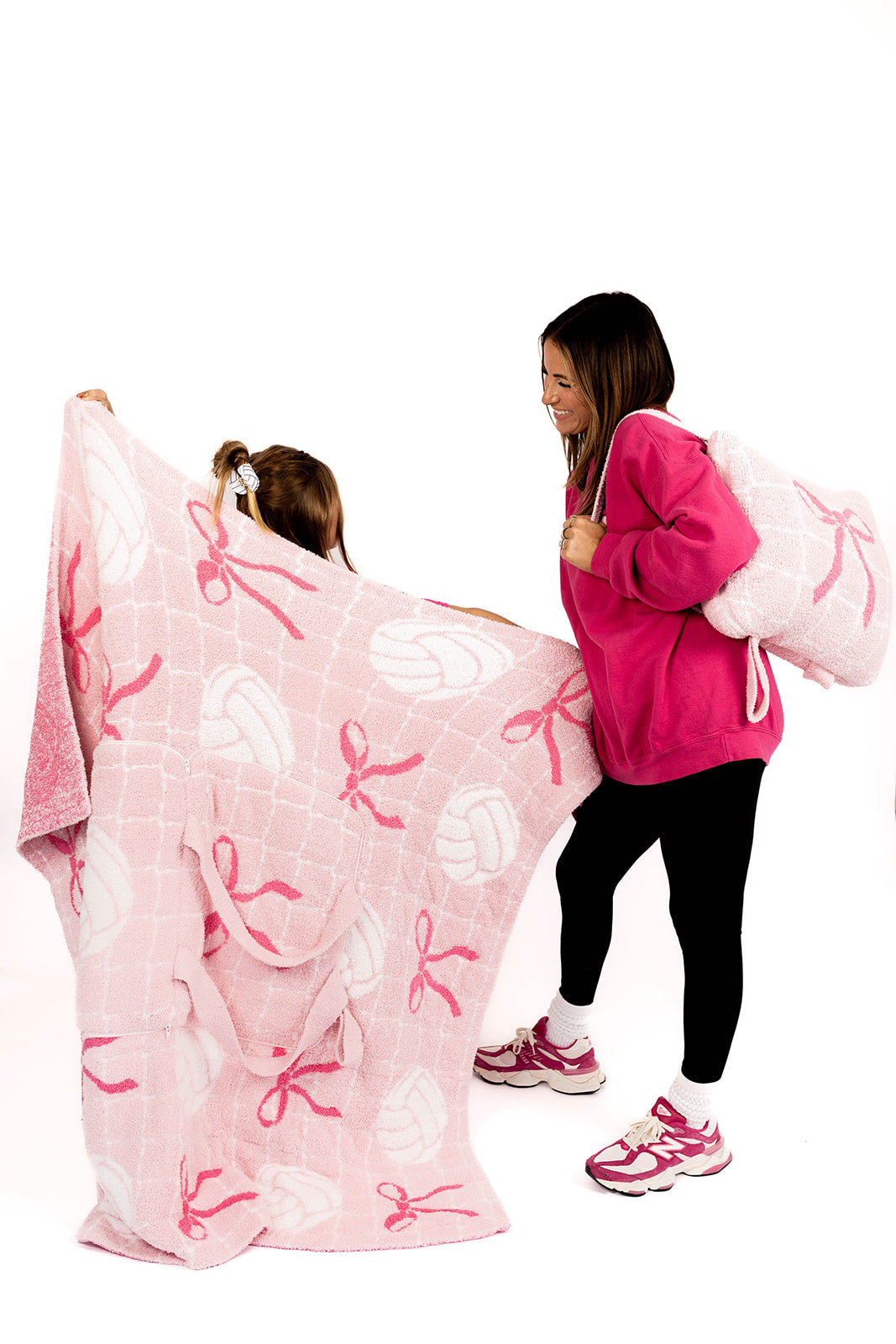 Two people with a pink blanket featuring white volleyballs and pink bows on a white background