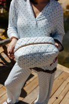 Model holding the blue and brown polka dot cosmetic bag.
