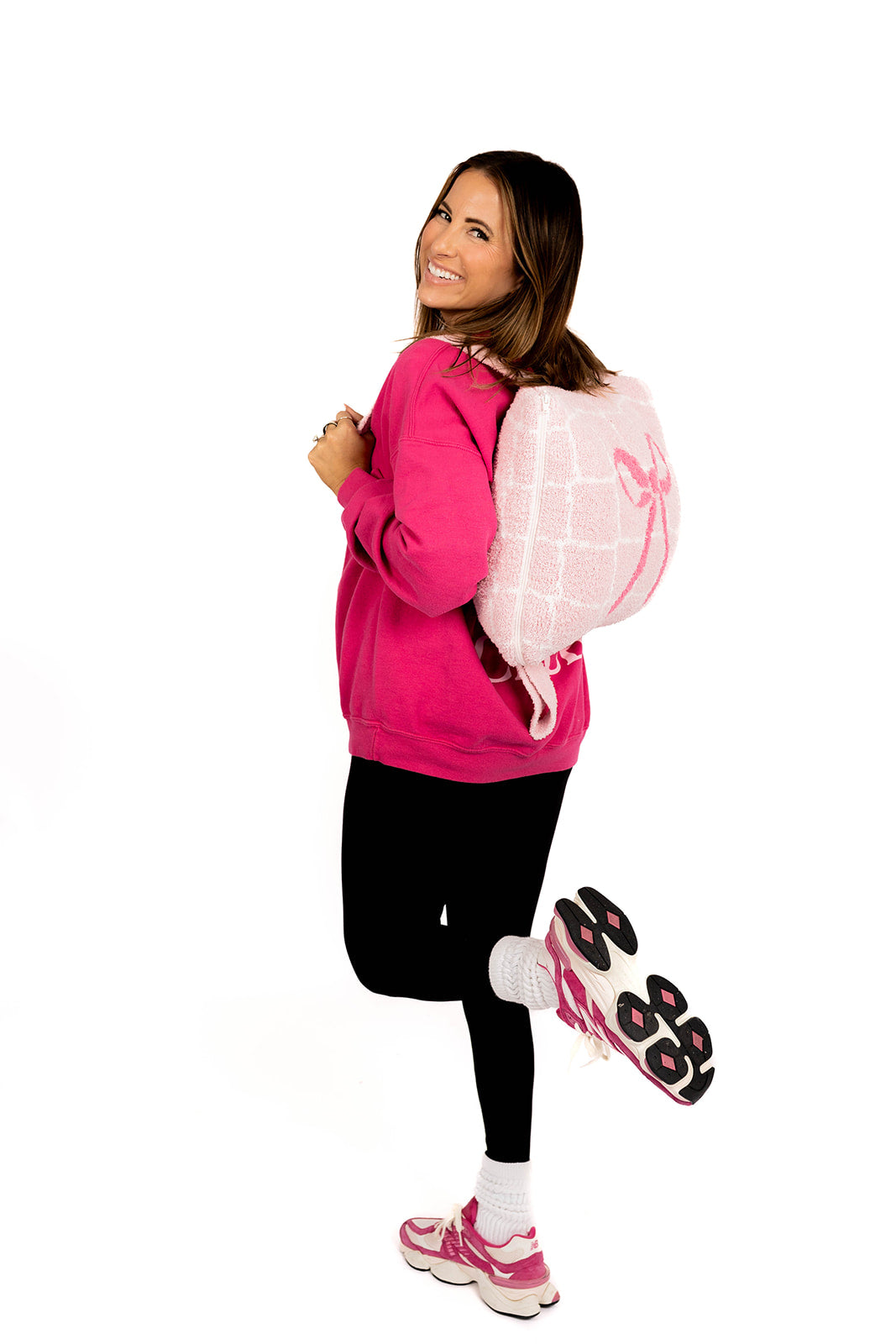 Woman wearing a pink sweatshirt, black leggings, and pink sneakers on a white background wearing volleyball quillow
