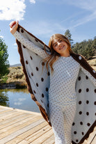 Model displaying the blue and brown polka dot quillow blanket outdoors.
