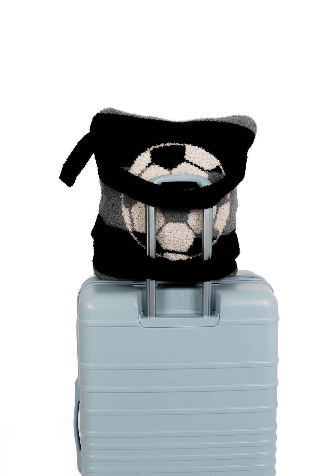 Light blue suitcase with a black and white patterned soccer quillow with straps on a white background 