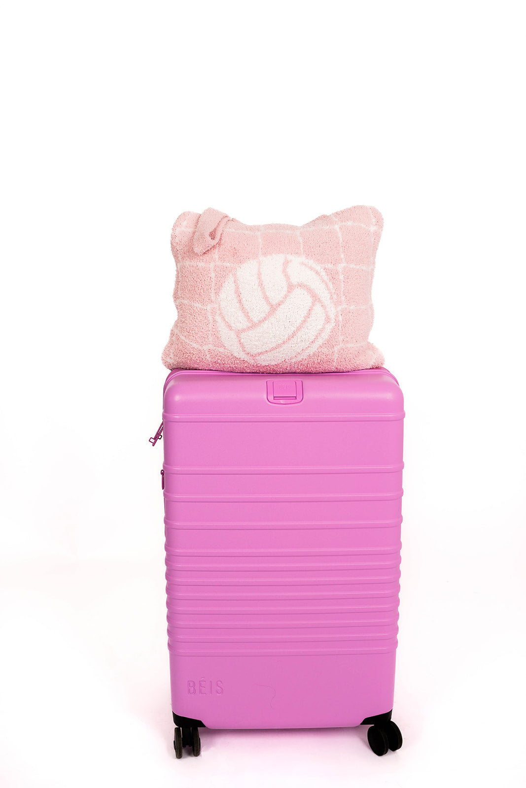 Pink suitcase with a pink volleyball quillow on top against a white background