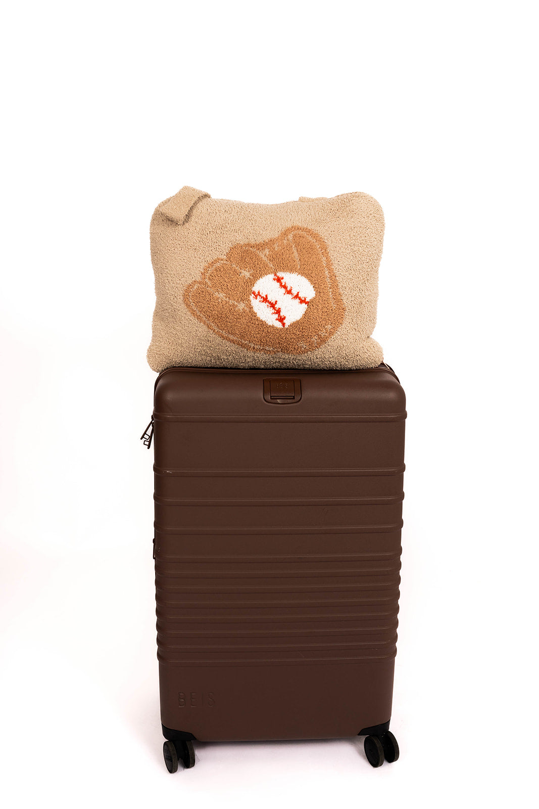 Brown suitcase with a baseball-themed quillow on top against a white background