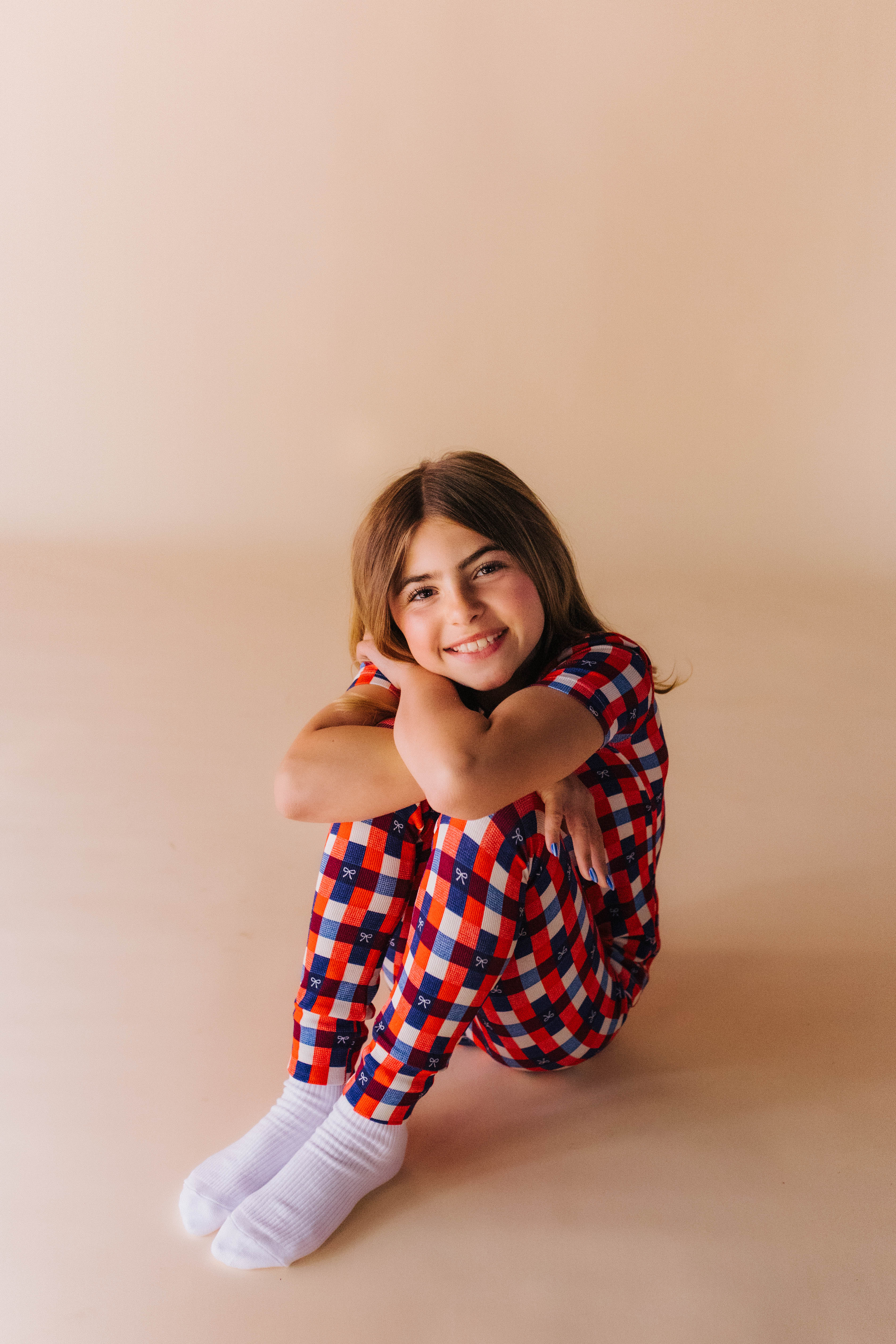 Person wearing a red, blue, and white gingham outfit sitting on a beige background