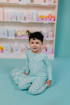 Child wearing a check onesie on a blue floor in front of shelves with products.