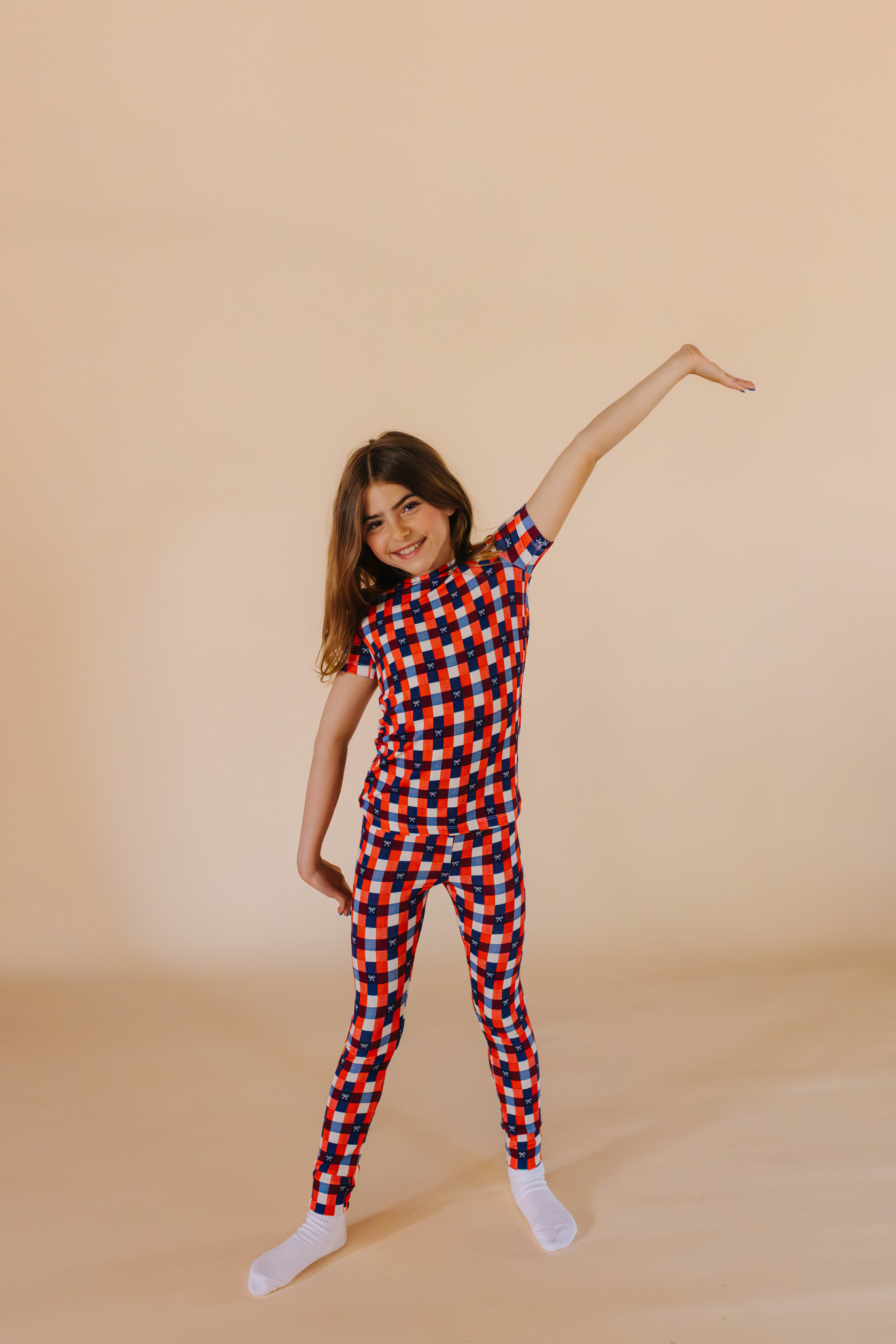 girl posing in gingham two piece pj set in front of cream background