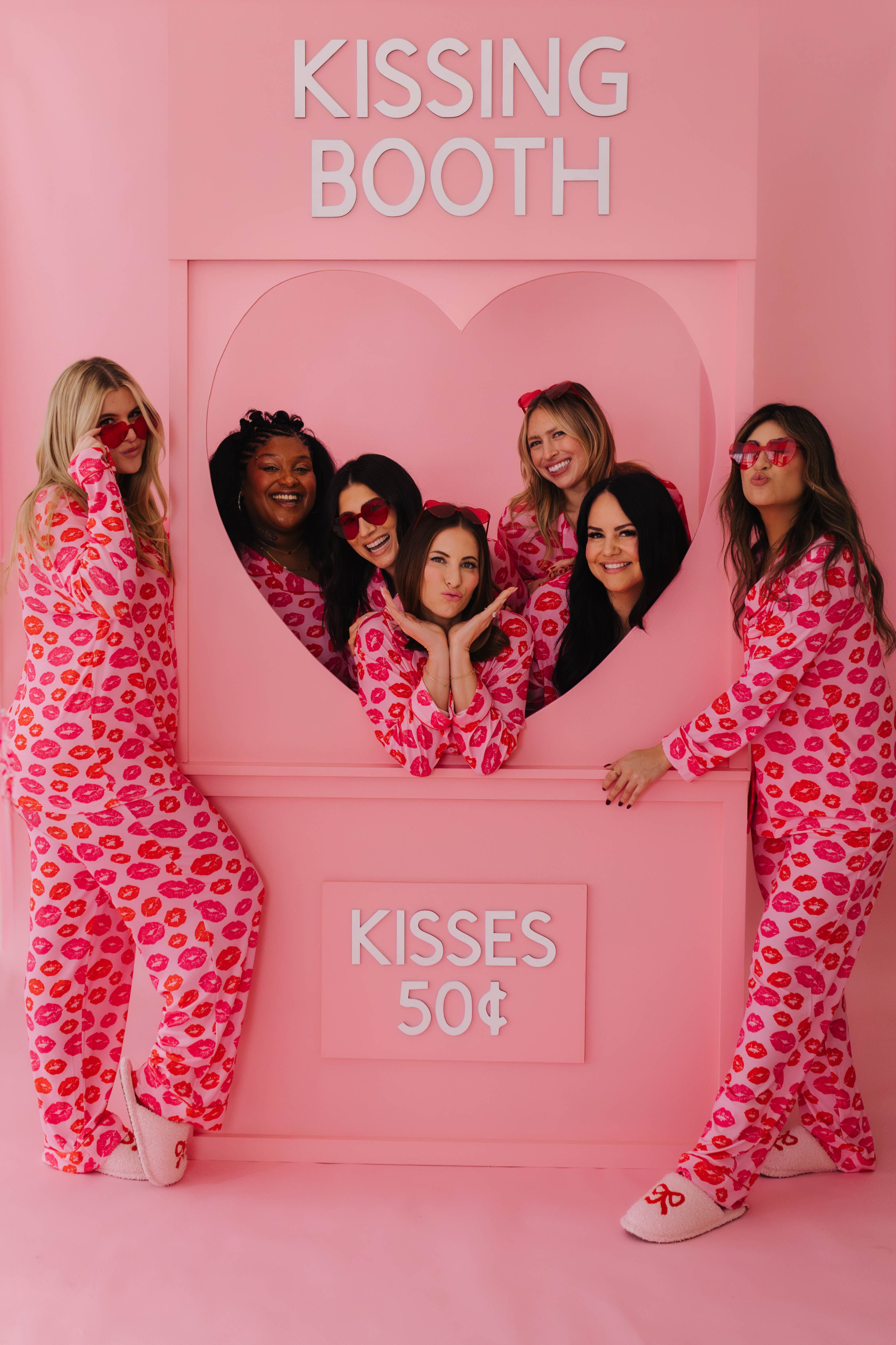 Pink 'Kissing Booth' themed photo booth with people in matching outfits.