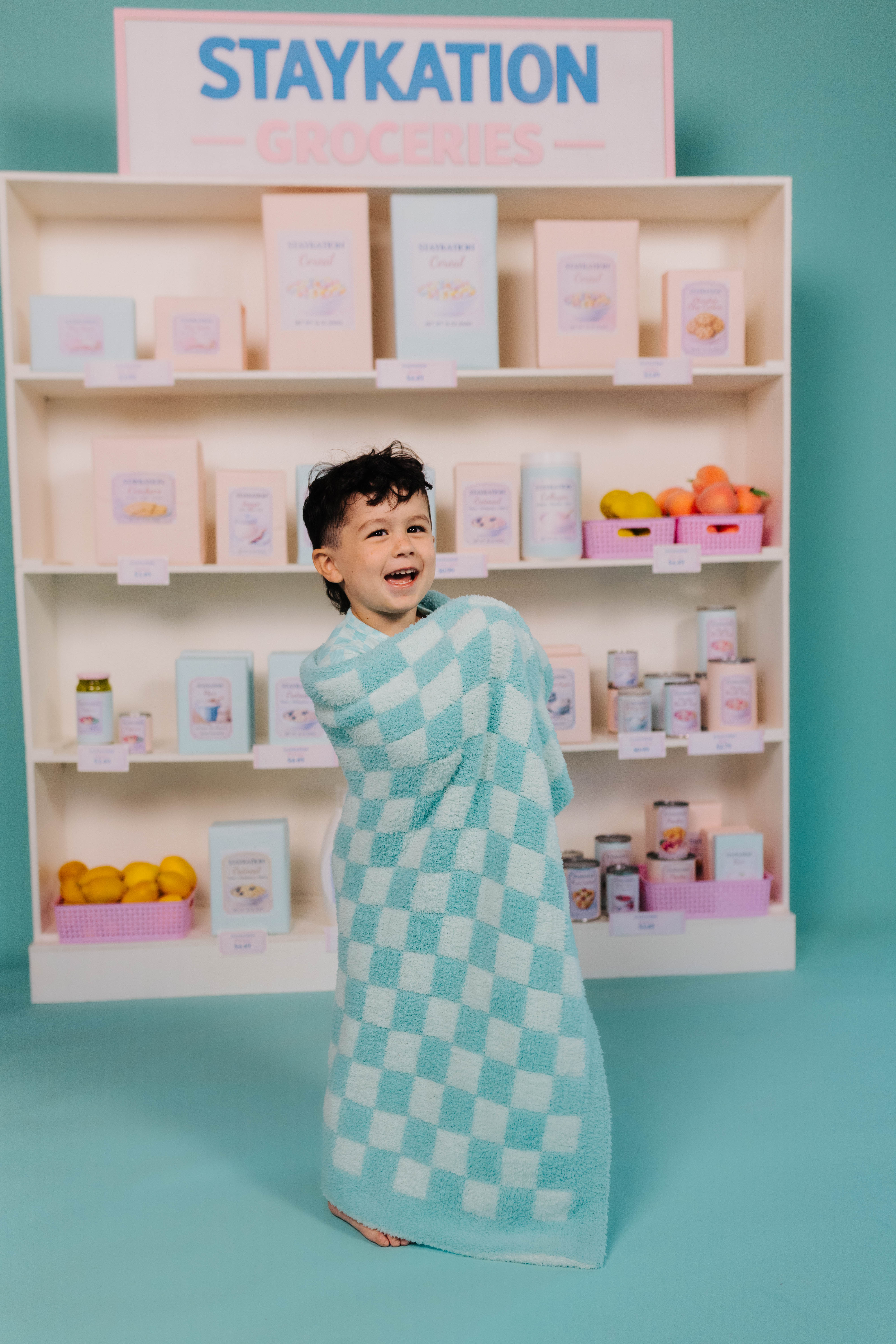 Child in a checkered blanket standing in front of a display with 'STAYKATION' sign