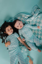 Two children in matching pajamas lying on a checkered blanket against a teal background