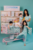 Family with children playing with a toy shopping cart against a teal background