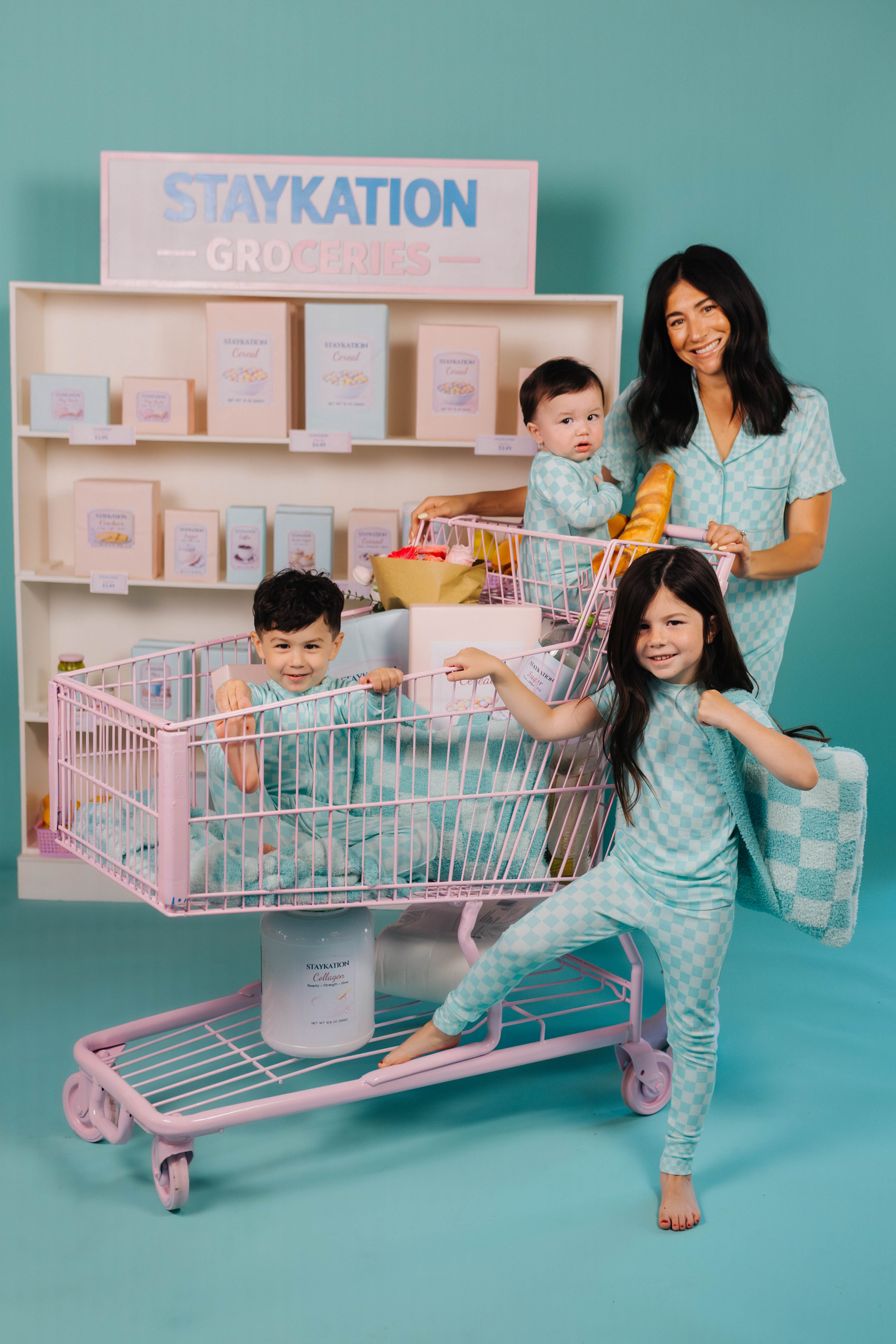 Family with children playing with a toy shopping cart against a teal background